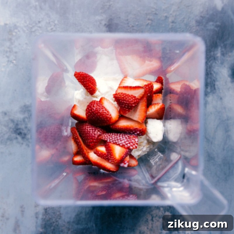 All fresh ingredients for strawberry milkshake being added to a high-speed blender.