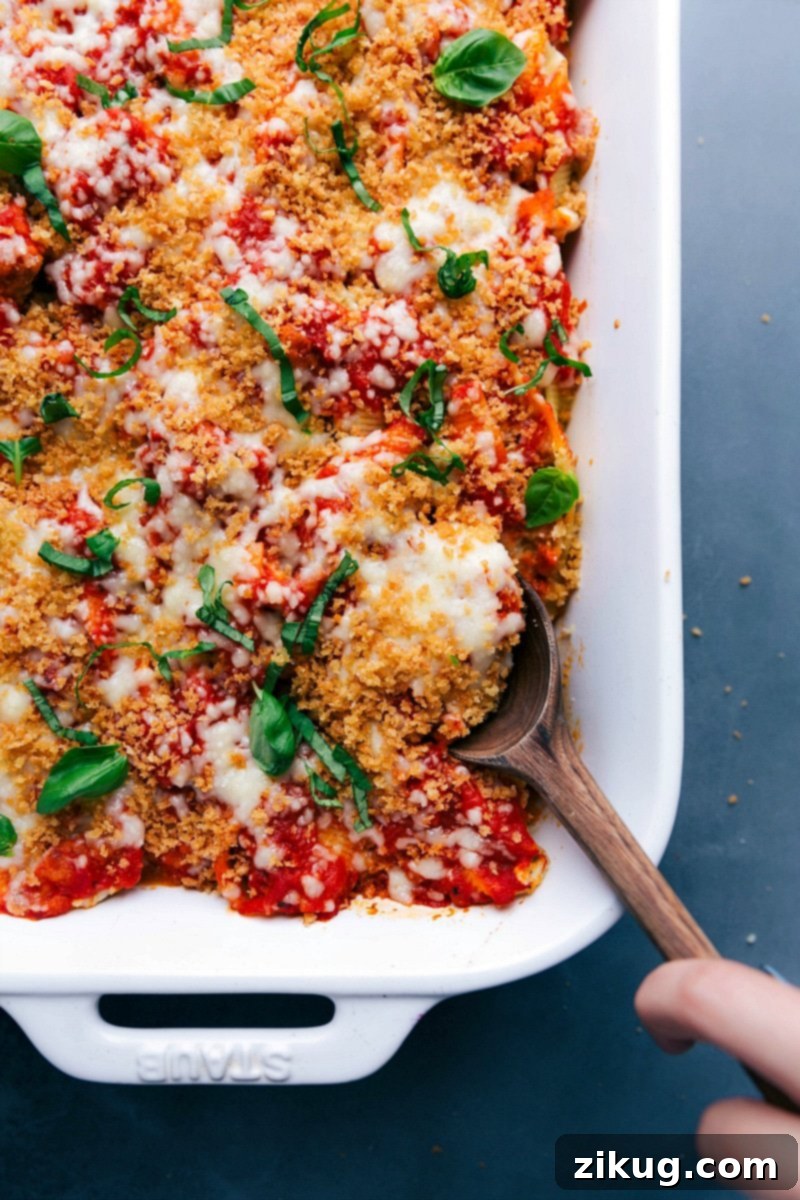 Hearty Meal Ready to Enjoy, with a Scoop Taken A finished, warm, and hearty meal of Chicken Parm Stuffed Shells, with a scoop being taken from the baking dish, showing the layers of pasta, cheese, and chicken.