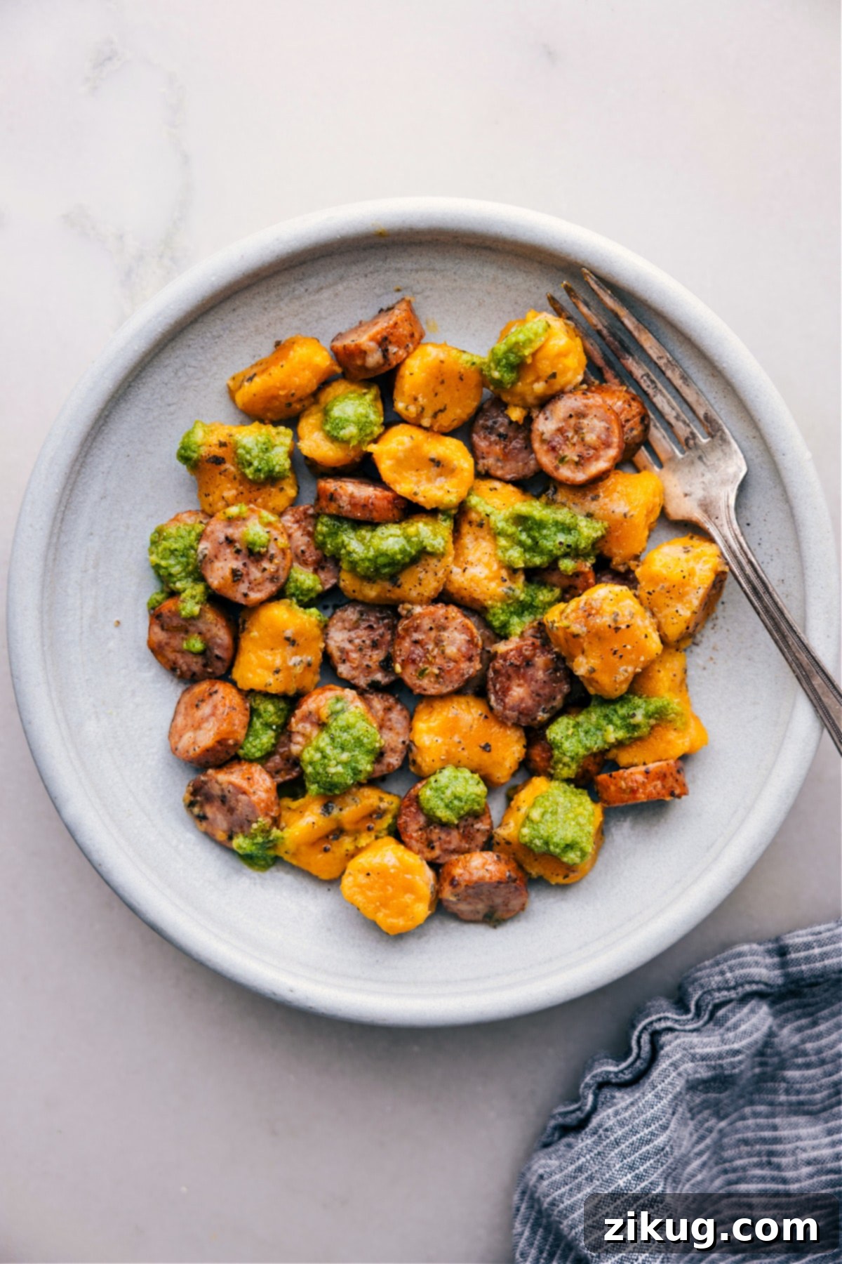 Easy Trader Joe's 3-Ingredient Recipes 5 A vibrant, plated serving of roasted sweet potato gnocchi and chicken sausage, generously topped with fresh basil pesto and a garnish of fresh basil leaves.