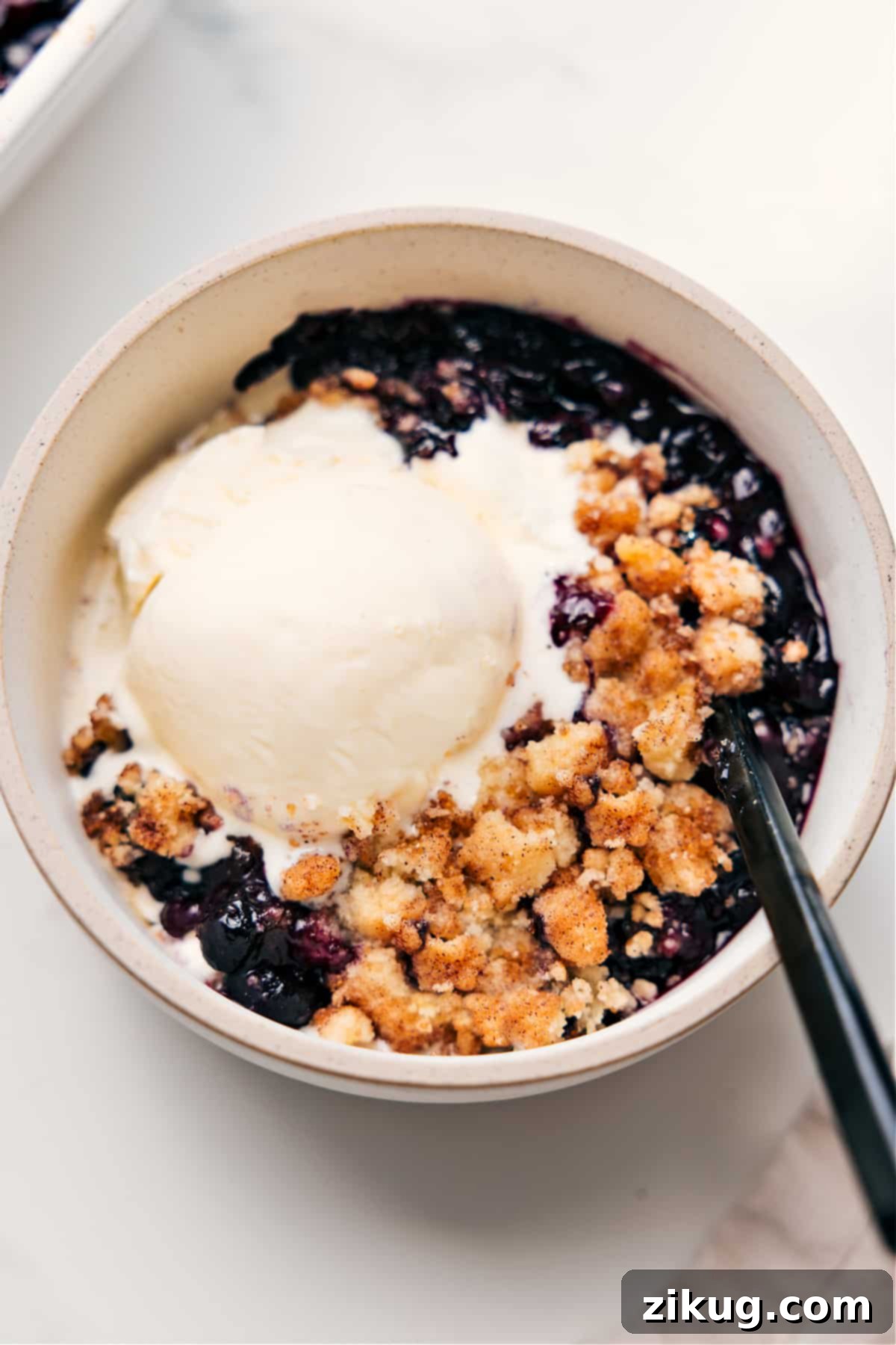 The Ultimate Award-Winning Blueberry Cobbler Recipe Delicious Blueberry Cobbler Recipe served warm in a bowl with a melting scoop of vanilla ice cream on top, ready to be enjoyed.