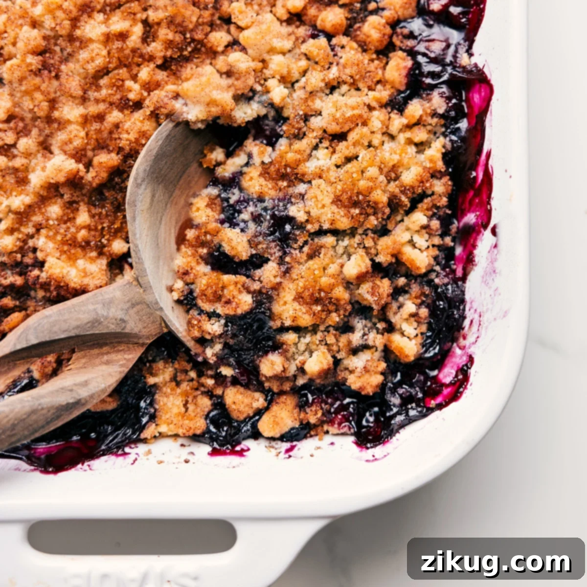 My Absolutely Favorite Blueberry Cobbler Recipe A close-up of a freshly baked blueberry cobbler, still warm in its dish, with a serving spoon taking out a generous portion, revealing the luscious berry filling.