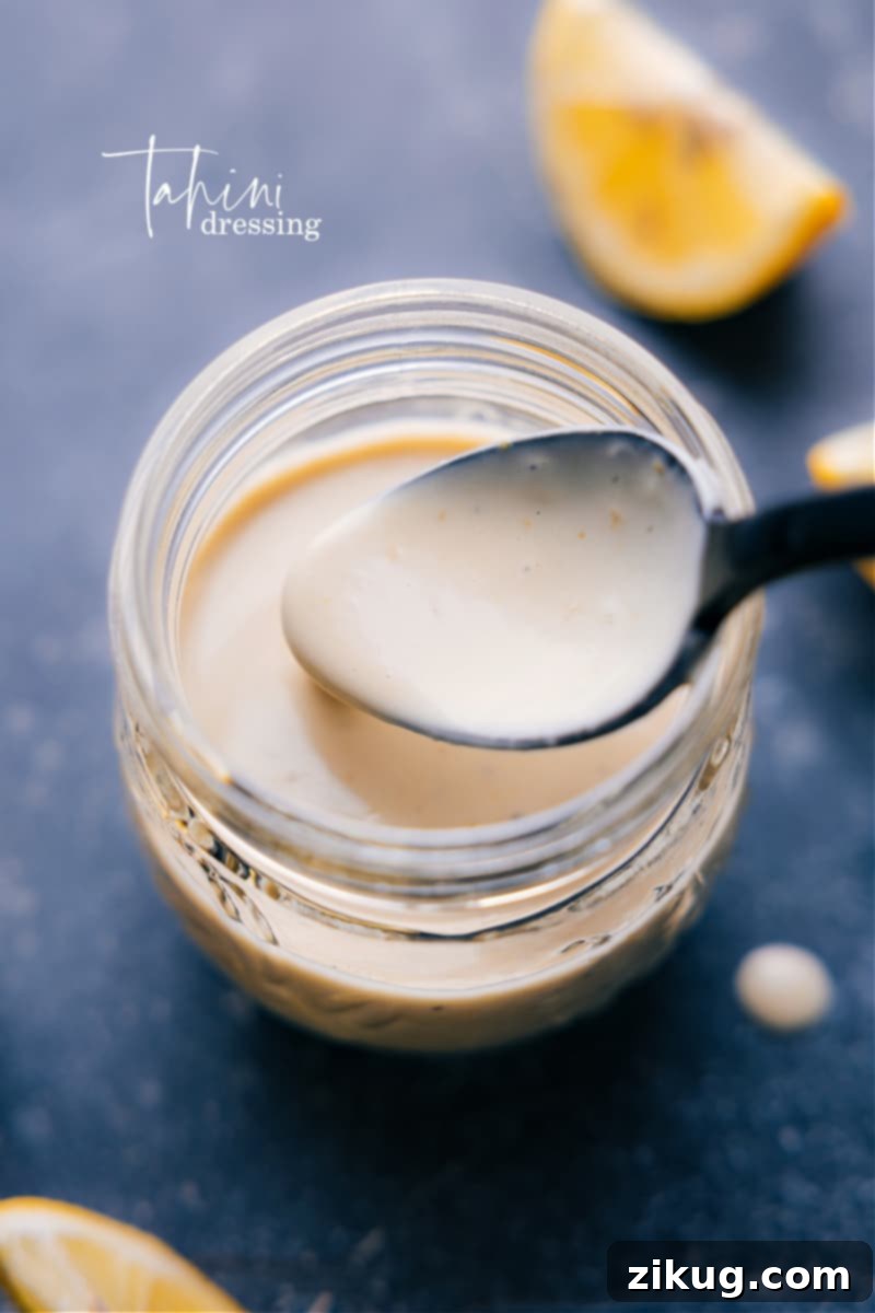 This homemade Tahini Dressing is luxuriously thick and creamy without any mayo or cream! It's delightfully flavored with a hint of lemon and touch of honey. Drizzle this dressing on your favorite salad. Recipe via chelseasmessyapron #salad #saladdressing #tahini #dressing Overhead image of freshly made Tahini Dressing in a jar, ready to be served, highlighting its creamy texture and rich color.