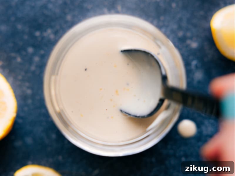 This Tahini Dressing is luxuriously thick and creamy! It's delightfully flavored with a hint of lemon and touch of honey. Drizzle this dressing on your favorite salad. Recipe via chelseasmessyapron #salad #saladdressing #tahini #dressing Overhead image of a prepared bowl of Tahini Dressing, garnished with a sprig of fresh herb, ready to be enjoyed as part of a healthy meal.