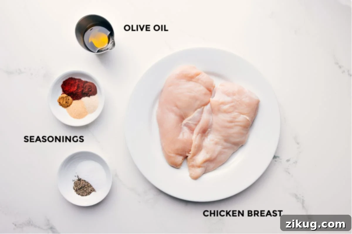 Essential Ingredients for Our Simple and Delicious Baked Chicken Breast Recipe All the fresh ingredients meticulously prepped for easy assembly, including boneless, skinless chicken breasts, a bottle of olive oil, and a selection of dried herbs and spices in small bowls.