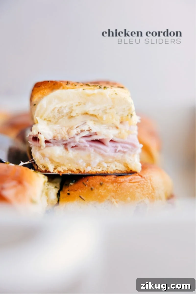 These Chicken Cordon Bleu Sliders pack a serious flavor punch! You get sweet Hawaiian rolls filled with savory ham, gooey Swiss cheese and juicy chicken, jazzed up with a tangy-sweet honey mustard sauce and garlicky butter – they're seriously delicious! Recipe via chelseasmessyapron #dinner #quick #easy #simple #familyfriendly #kidfriendly #onepan #appetizer #chickencordonbleu #sliders A tray of golden-brown Chicken Cordon Bleu Sliders, freshly baked with melted cheese and a glistening butter topping