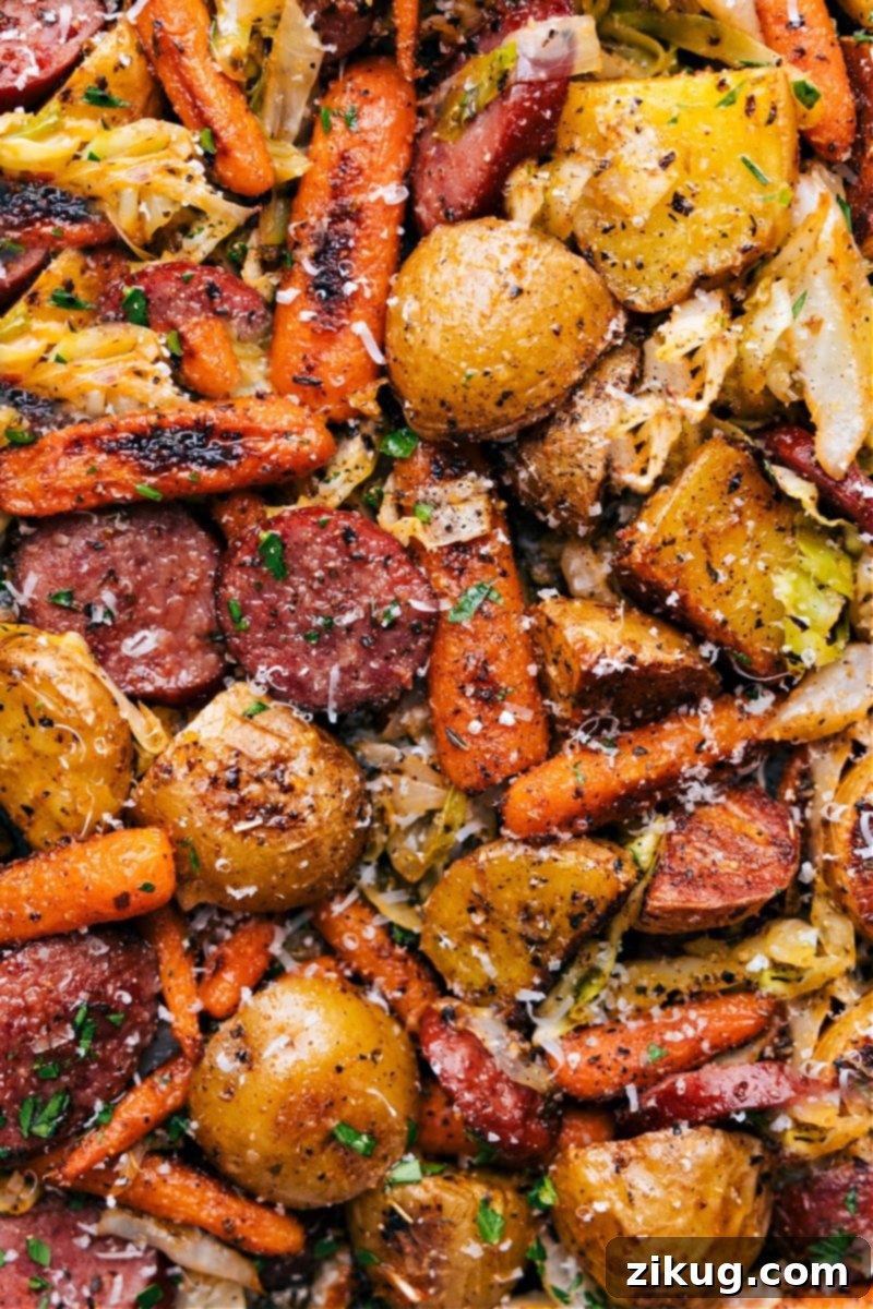 Our favorite Cabbage, Potatoes, and Sausage, perfectly roasted and ready to enjoy, finished with a creamy Dijonnaise and fresh Parmesan. Beautiful overhead shot of the finished One-Pan Cabbage, Potatoes, and Sausage dinner, garnished generously with fresh parsley and ready to be served, still steaming hot from the oven.