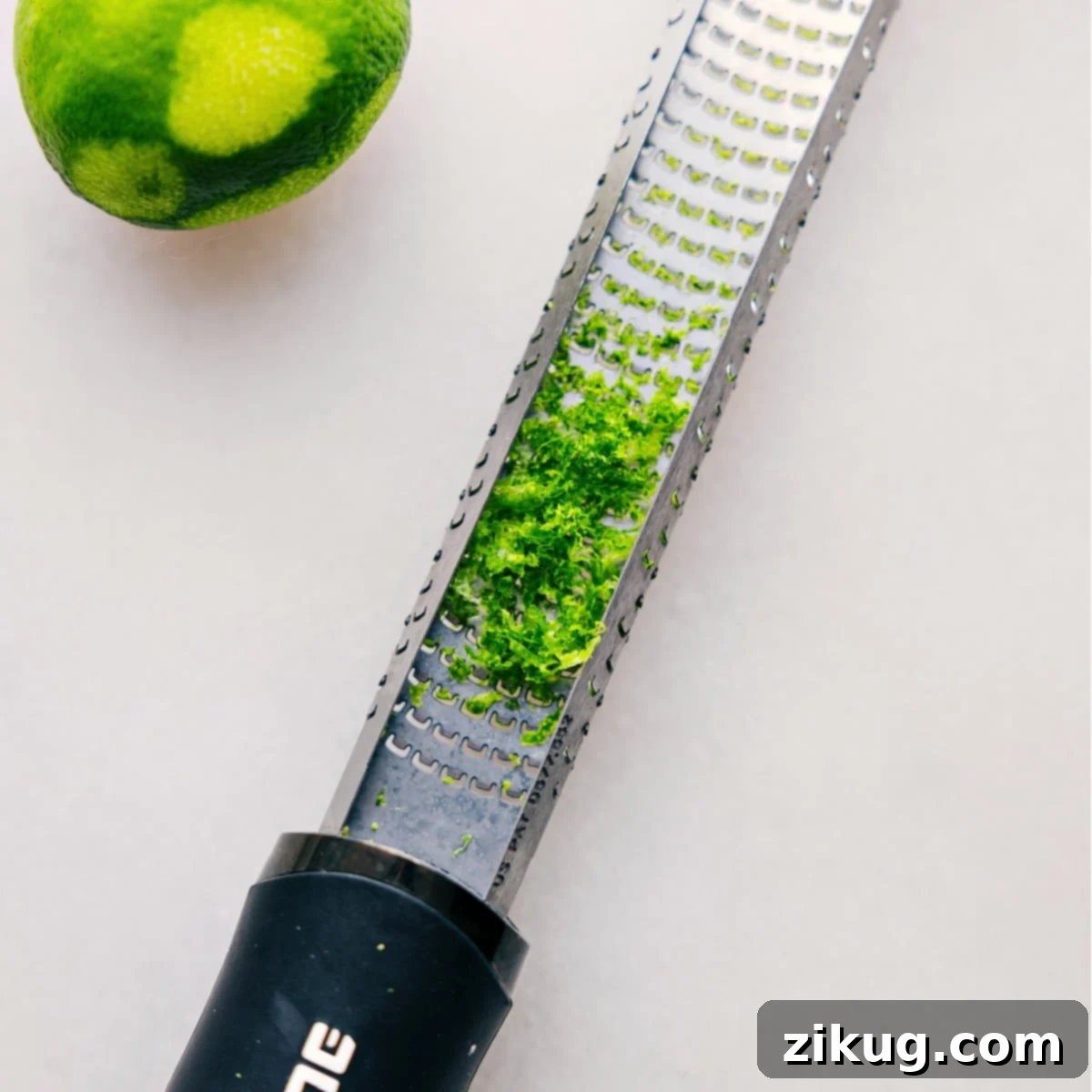 Fresh Lime Zest: Unlocking Vibrant Citrus Flavors with a Zester! A microplane zester covered in vibrant green lime peel shavings, demonstrating the fresh zest extracted from a lime, essential for adding bright citrus flavor to the sauce.