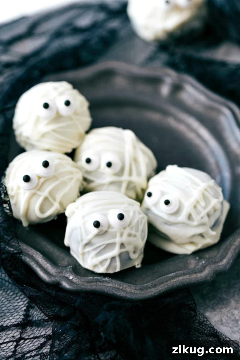 Spooktacular Oreo Truffles 6 White chocolate mummy Oreo balls with crisscrossing 'bandages' and edible candy eyes peeking out, adding a ghostly touch to Halloween desserts.