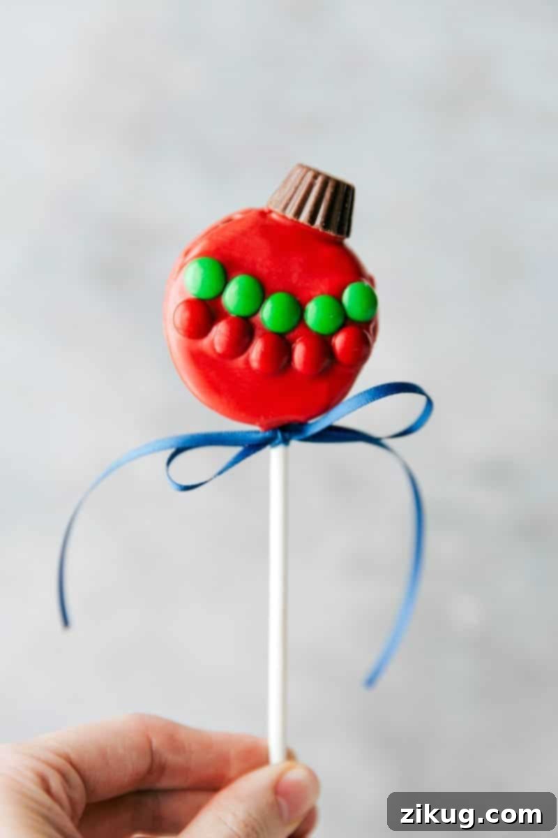 Adorable ornament Oreo pops decorated for Christmas. Image of the vibrant red ornament Oreo pop topped with a miniature Reese's cup and M&M's.