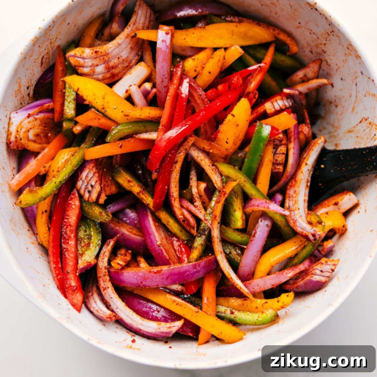 How To Make Sheet Pan Chicken Fajitas Finely chopped colorful bell peppers and thinly sliced red onions are generously tossed with the vibrant homemade fajita seasoning mix in a large stainless steel mixing bowl, showcasing the preparatory stage for these delicious sheet pan chicken fajitas.