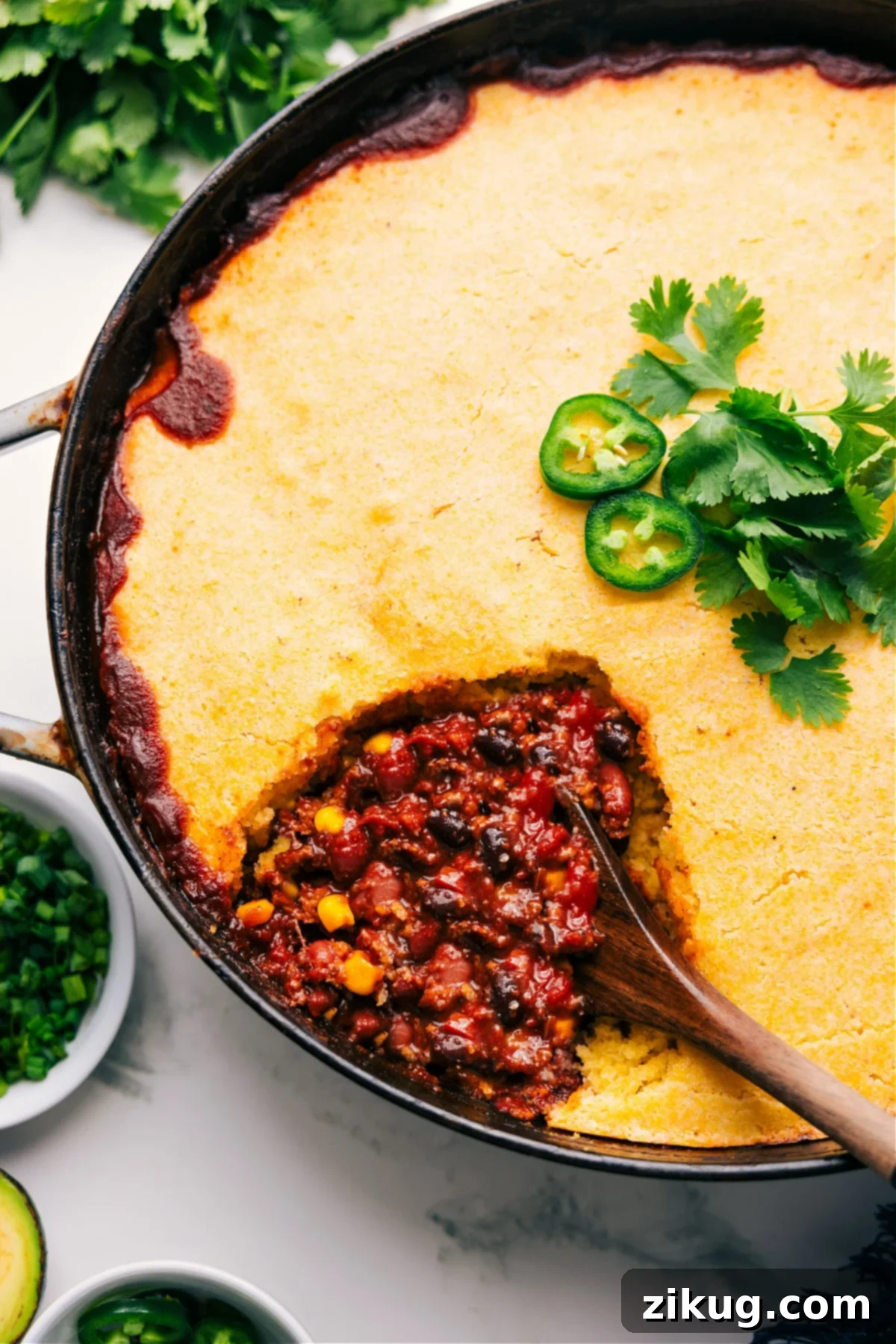 Skillet Cornbread Casserole Recipe That's Pure Comfort Food Perfection A large skillet filled with golden-brown cornbread casserole, with a generous scoop lifted out, revealing the rich beef chili beneath.