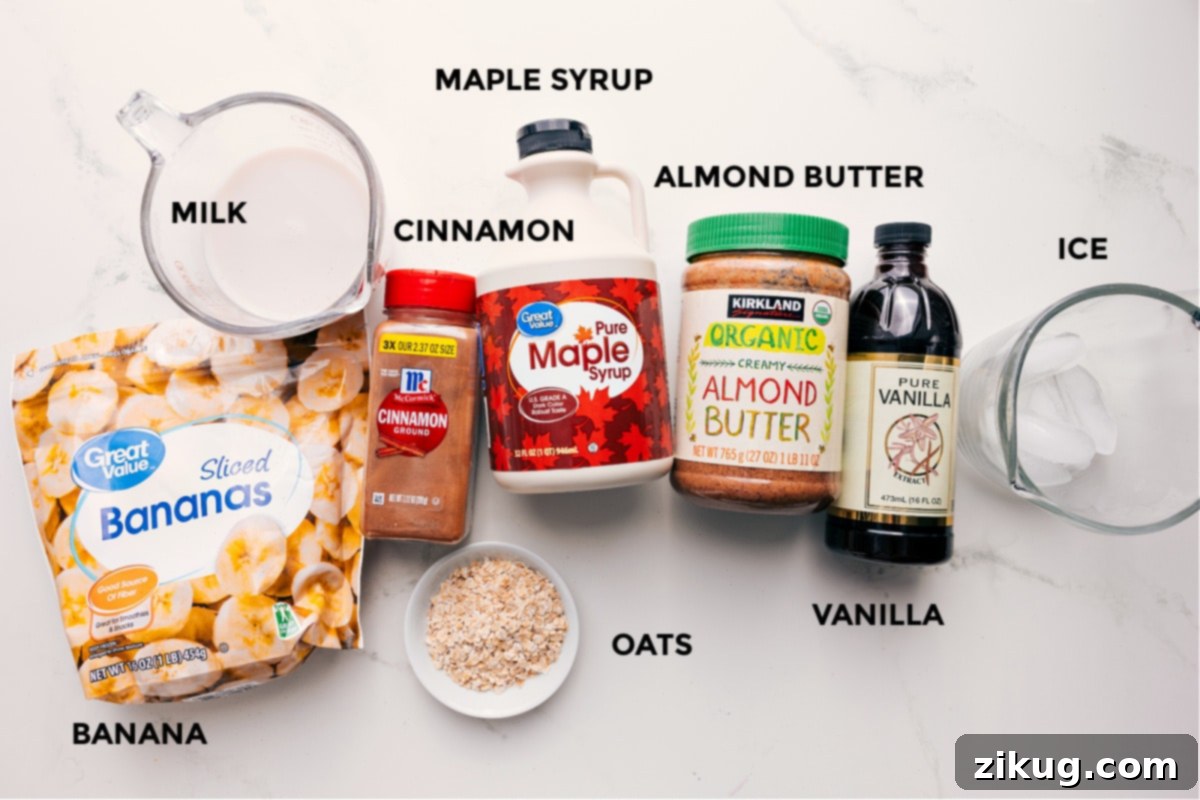 Essential Ingredients For Your Oatmeal Smoothie All the fresh ingredients for an oatmeal smoothie are neatly prepped and displayed on a white surface, including sliced frozen bananas, a bowl of old-fashioned oats, almond milk, almond butter, maple syrup, ground cinnamon, vanilla extract, a pinch of salt, and ice cubes.