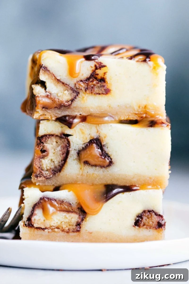 Delicious Twix Cheesecake Bars with caramel and chocolate toppings Stack of three Twix Cheesecake Bars, showcasing the layers of crust, cheesecake, Twix, caramel, and chocolate ganache.