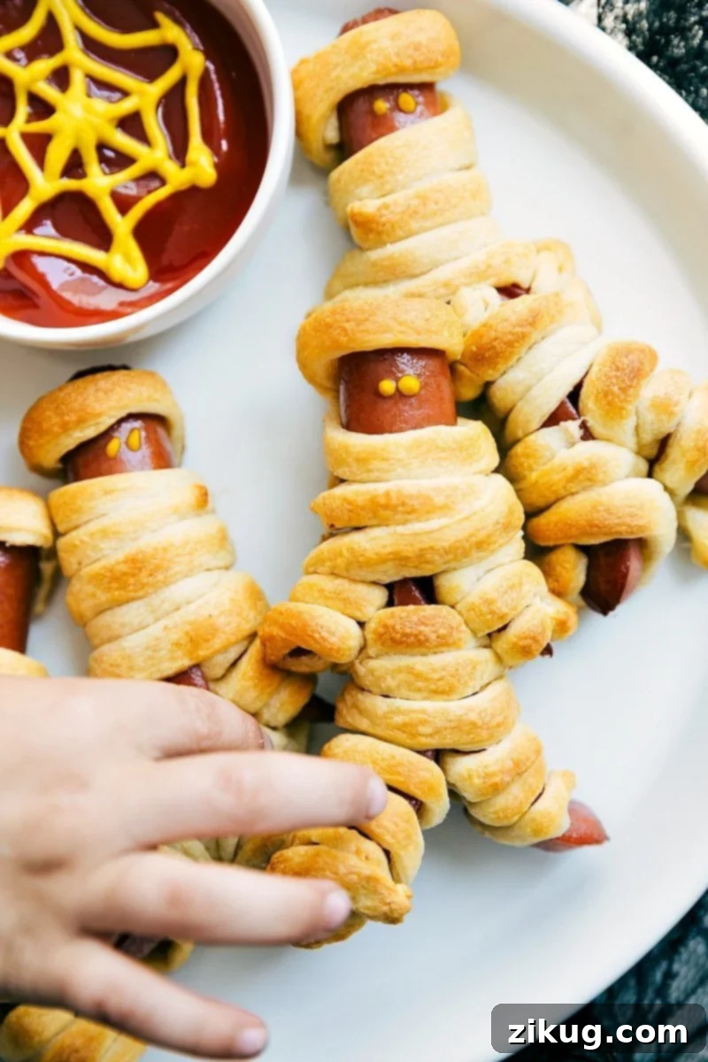 Four easy, & creative Halloween party appetizers that are so delicious -- Spiderweb 7-Layer Dip, Walking Dead Mummy Dogs, Monster Meatball Sliders, & Cheesy Monster Fingernail Bread. chelseasmessyapron.com #mummy #hotdog #mustard #halloween #treats #appetizer Image of the walking dead mummy dogs, a spooky Halloween appetizer for kids and adults