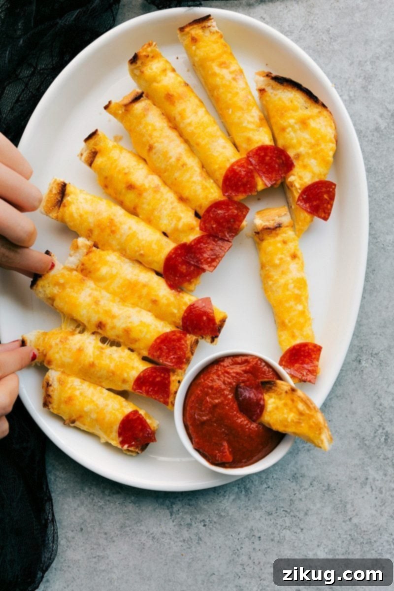 Four easy, & creative best Halloween appetizers that are so delicious -- Spiderweb 7-Layer Dip, Walking Dead Mummy Dogs, Monster Meatball Sliders, & Cheesy Monster Fingernail Bread. chelseasmessyapron.com Image of the Cheesy Monster Fingernail Bread, ready to eat and being dipped in marinara, a fantastic Halloween appetizer