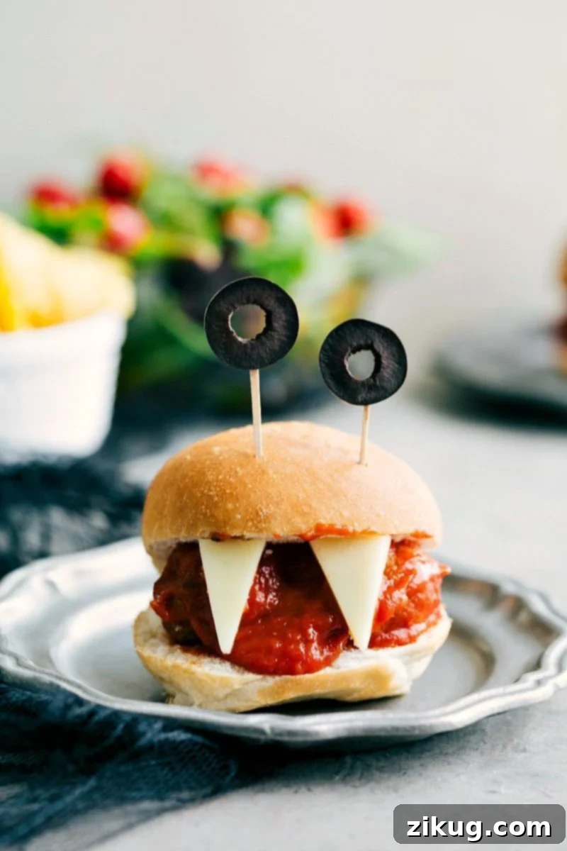 Monster Meatball Sliders: Four easy, & creative Halloween appetizers that are so delicious -- Spiderweb 7-Layer Dip, Walking Dead Mummy Dogs, Monster Meatball Sliders, & Cheesy Monster Fingernail Bread. chelseasmessyapron.com Image of the Monster Meatball Sliders with olive eyes and cheese teeth, an easy Halloween appetizer