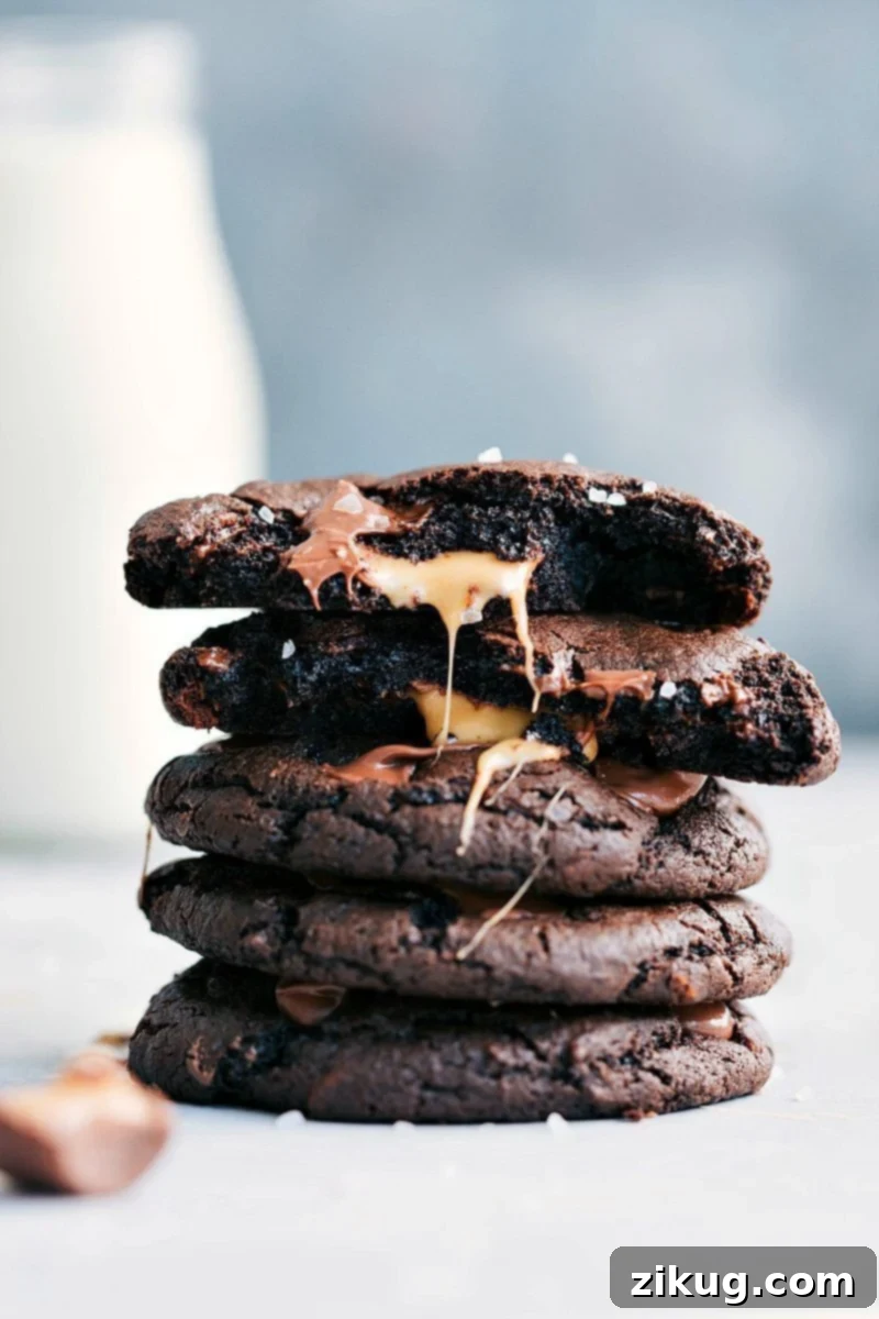 Bakery-style, soft and chewy, sweet Chocolate Caramel Cookies with a chocolate-covered caramel candy in the center and Maldon sea salt flakes on top! An irresistible dessert perfect for any occasion. A close-up image of two bakery-style Chocolate Caramel Cookies, one whole and one split to reveal the gooey caramel center, topped with flaky sea salt.