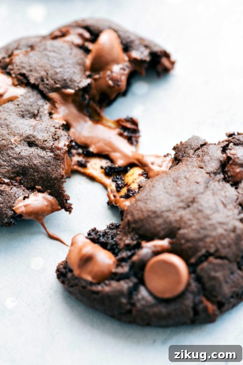 Sweet Chocolate Caramel Cookies with a chocolate-covered caramel candy in the center and Maldon sea salt flakes on top! Recipe via ChelseasMessyApron, revealing the irresistible gooey core. Close-up image of a chocolate caramel cookie split in half, clearly showing the melted, gooey Rolo caramel center and the rich chocolate cookie texture, topped with flaky sea salt.