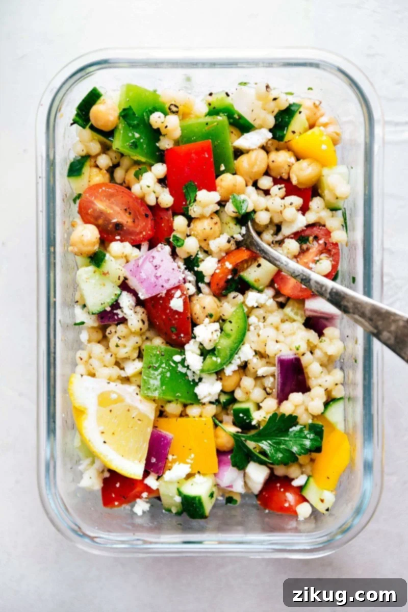 Greek Salad With Couscous For Dinner Greek couscous salad dressing being tossed with the salad, ready to be served with a fork