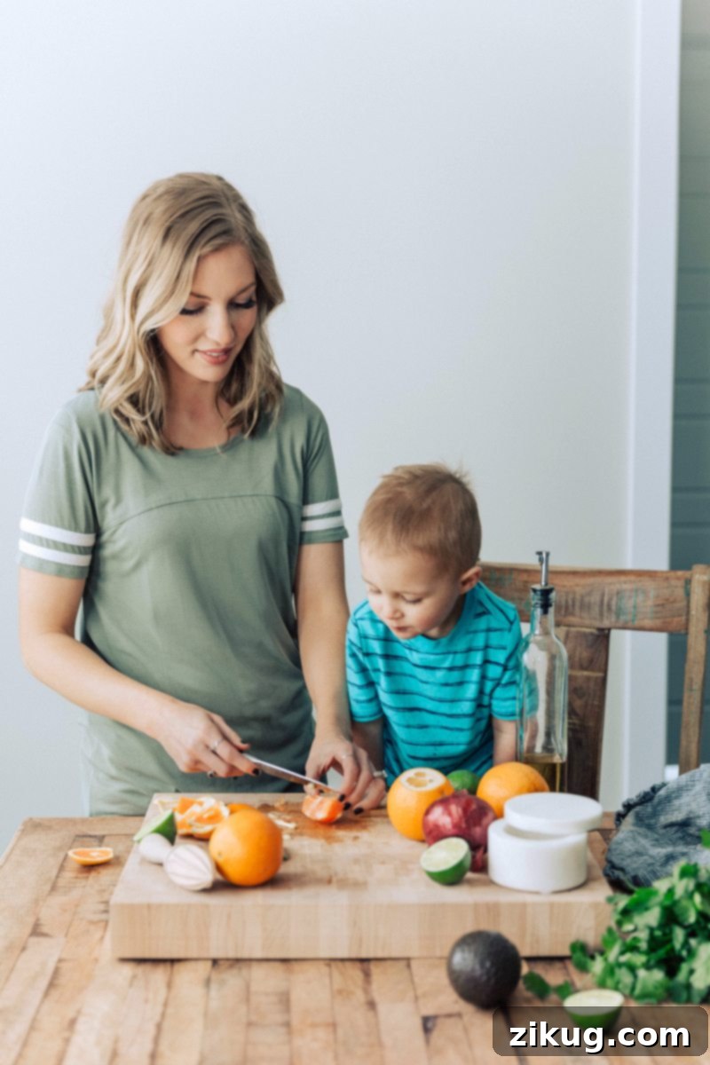 A family-friendly kitchen scene, showcasing the preparation of the delicious avocado citrus salsa to perfectly complement grilled mojo chicken. A healthy and easy recipe for everyone to enjoy. #avocado #citrus #salsa #easy #quick #dinner #rice #cilantro #lime #fresh #healthy #kidfriendly #cuban #mojo #chicken #dinner A home chef, possibly with a child, is seen dicing fresh oranges and avocados on a cutting board, preparing the vibrant citrus avocado salsa to accompany the Cuban Mojo Chicken. Fresh ingredients like cilantro and limes are also visible.