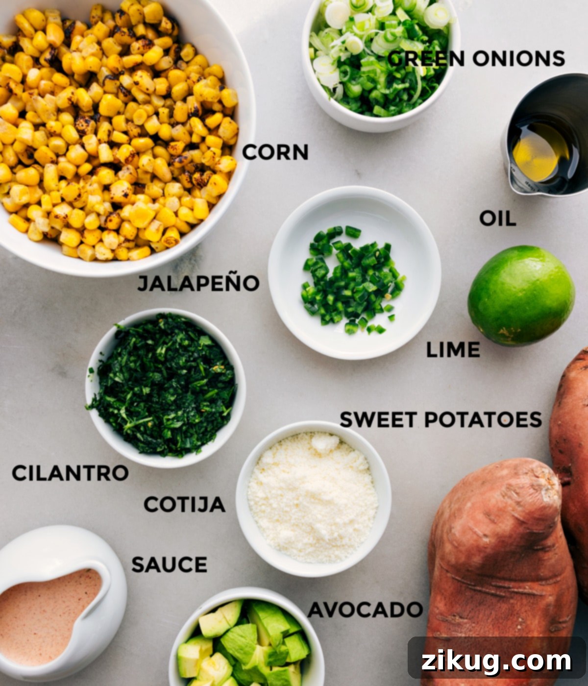 Key Ingredients for Delicious Loaded Sweet Potatoes All ingredients prepped and laid out for easy assembly of loaded sweet potatoes, including roasted corn, diced avocado, chopped green onions, fresh cilantro, jalapeño, lime, cotija cheese, olive oil, and sauce ingredients.