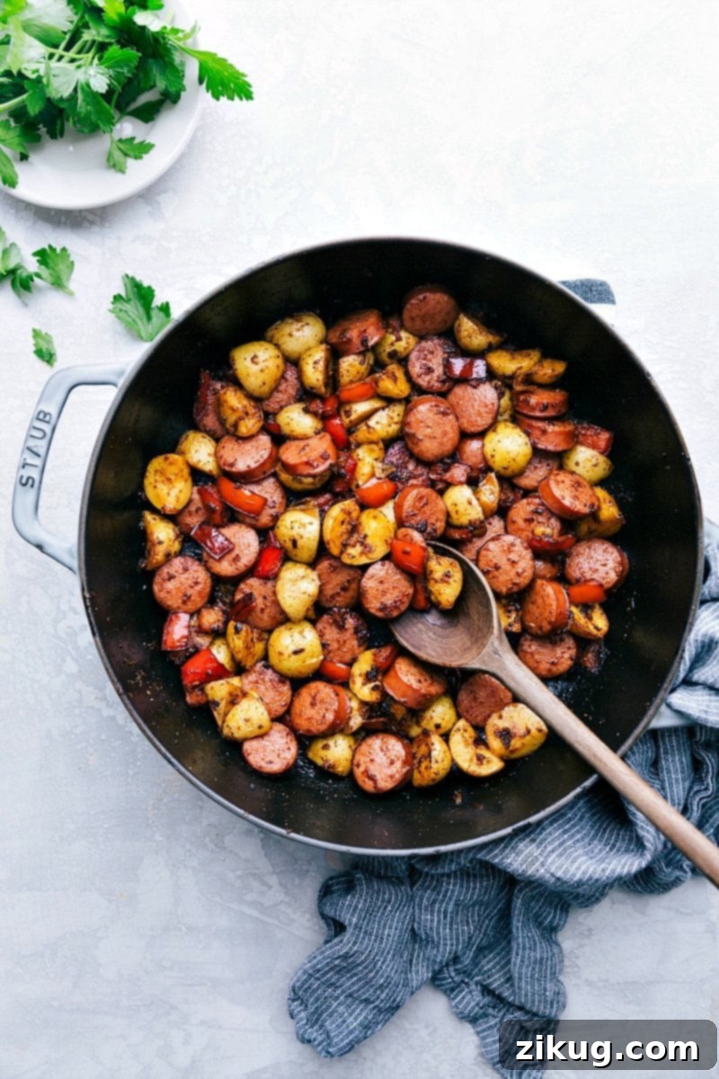 The easiest 20-minute Sausage and Potatoes Skillet Meal! This simple dinner can all be made in one pan and is loaded with flavor! Recipe via chelseasmessyapron #dinners #recipes #comfortfoods #simple #keilbasa #meals #healthy #sausage #onepanmeal #potatoes #quick Overhead photo of a vibrant Sausage and Potatoes Skillet Meal, featuring golden-brown potatoes, sliced smoked sausage, and colorful bell peppers, garnished with fresh herbs.