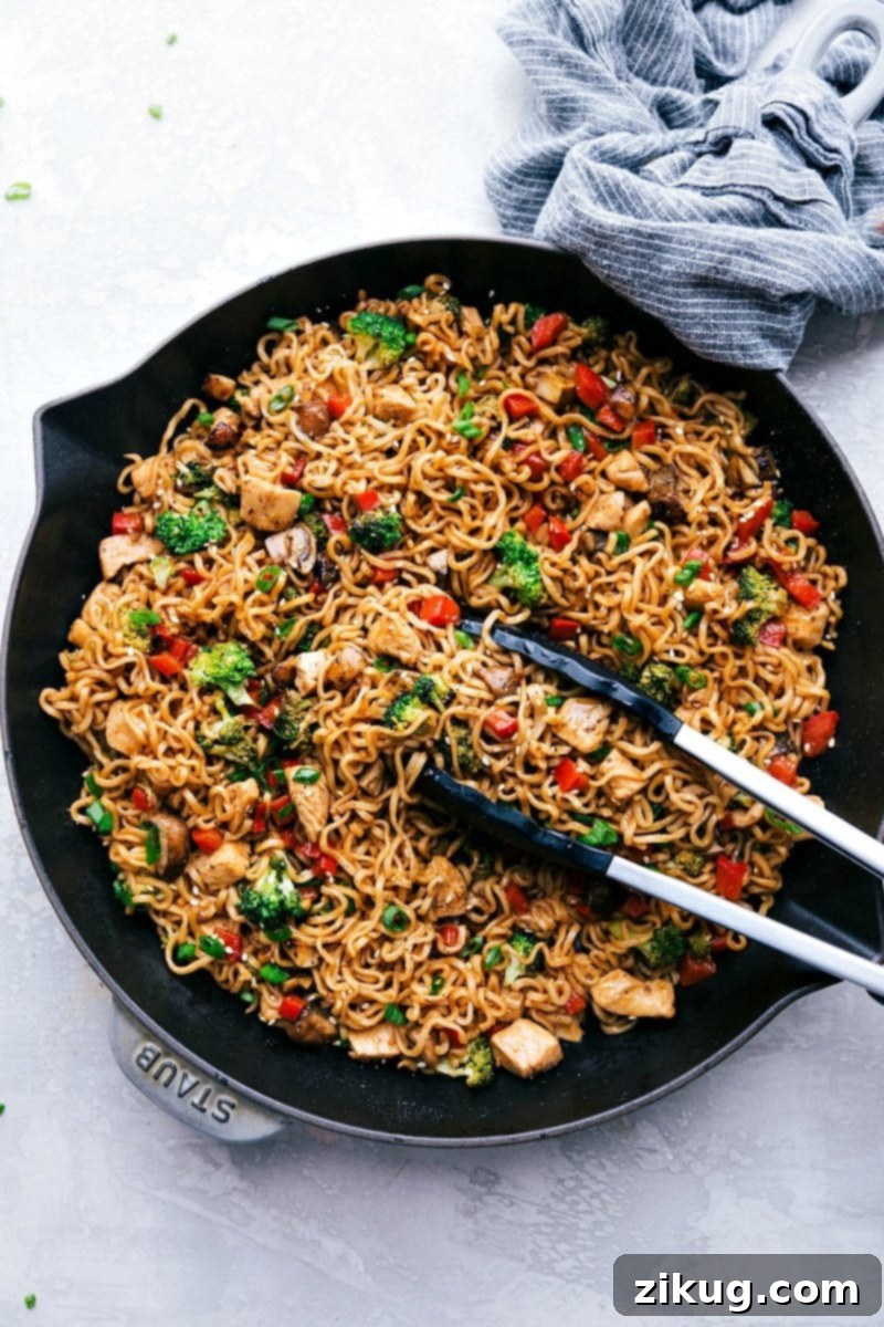 Quick 30-Minute Chicken Ramen Recipe Tongs gently lifting a tangle of saucy Chicken Ramen noodles from a skillet, showcasing the vibrant chicken and vegetables.