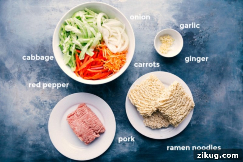 Assortment of ingredients for egg roll noodle recipe, including cabbage, red pepper, onion, carrots, ramen noodles, ground pork, garlic, and ginger.