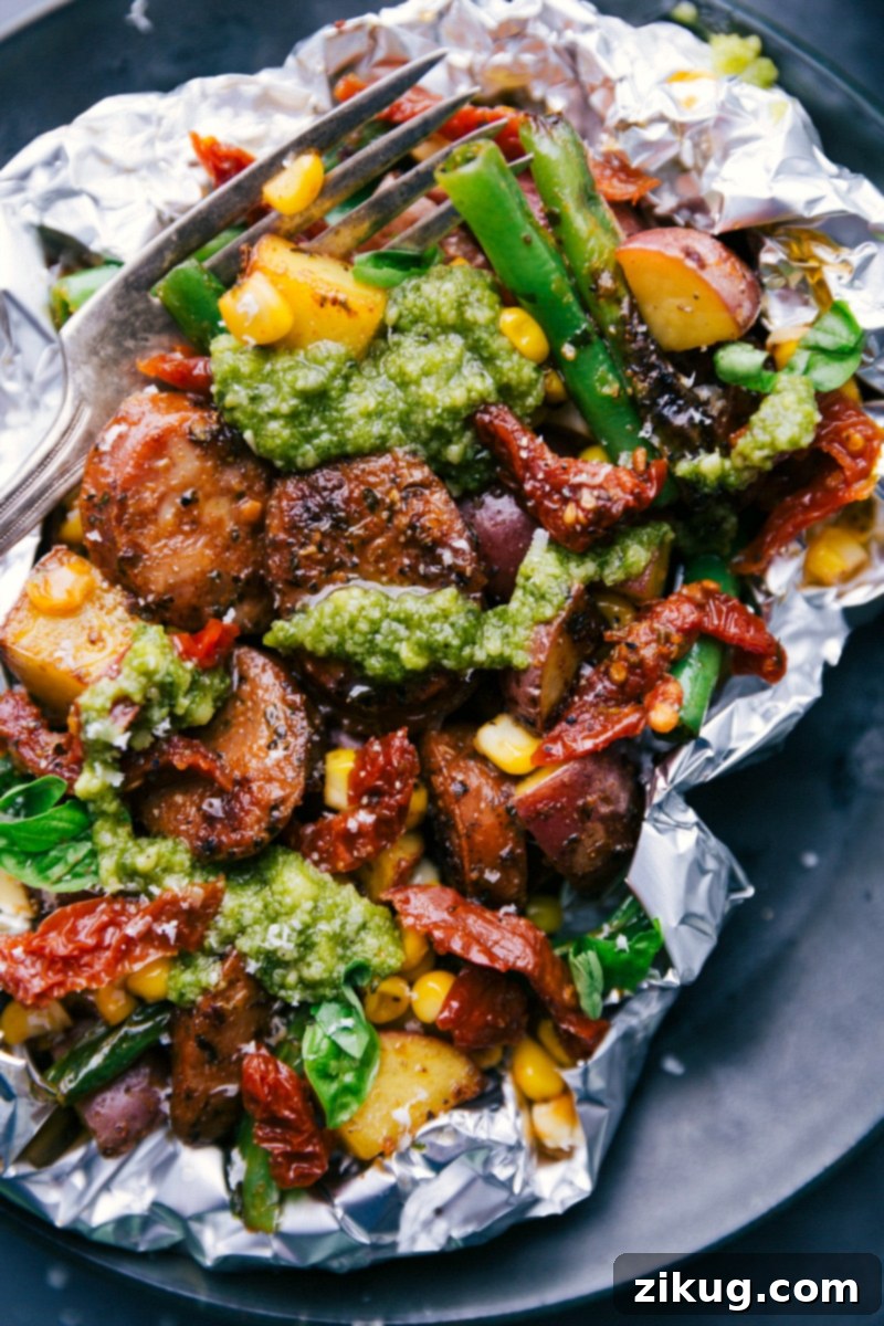 Foil Pack Feast: Fresh Pesto Topping Over Robust Ingredients A hearty foil pack dinner generously topped with fresh pesto, beautifully revealing its savory chicken sausage, potatoes, and vegetables within.