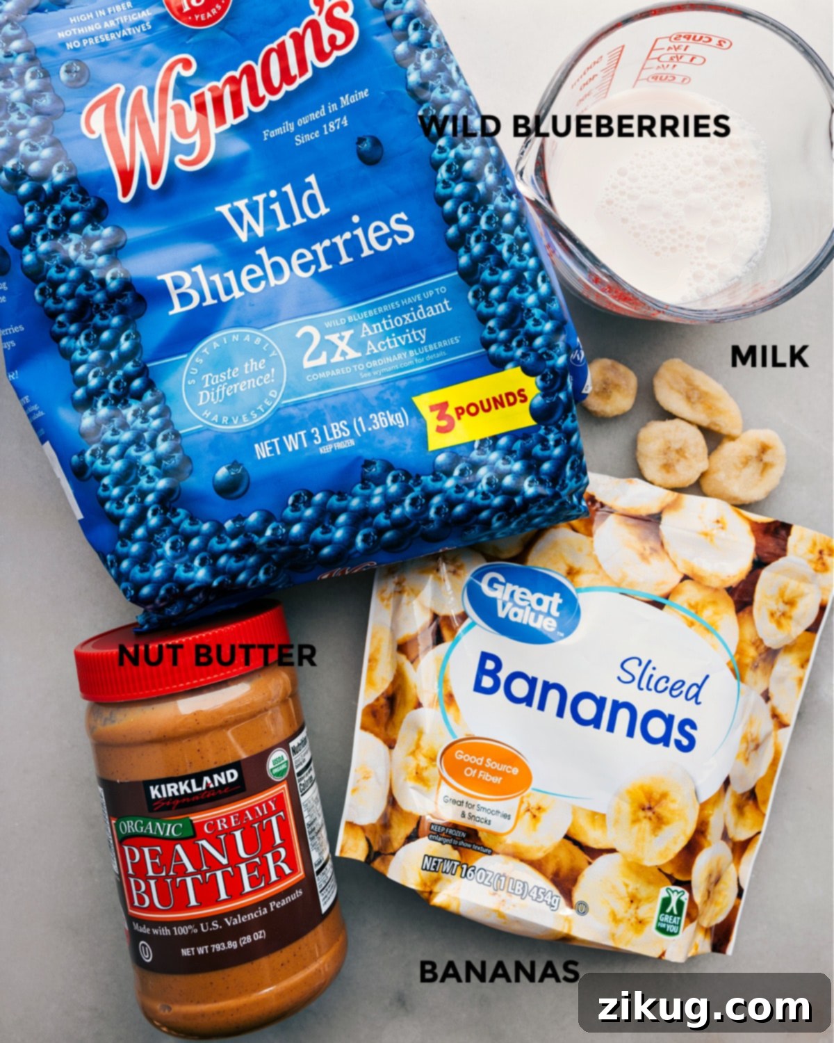 The Simple Four Ingredients In This Delicious Blueberry Smoothie Four essential ingredients for a blueberry smoothie: frozen blueberries, sliced frozen banana, almond milk, and almond butter, neatly arranged for preparation.
