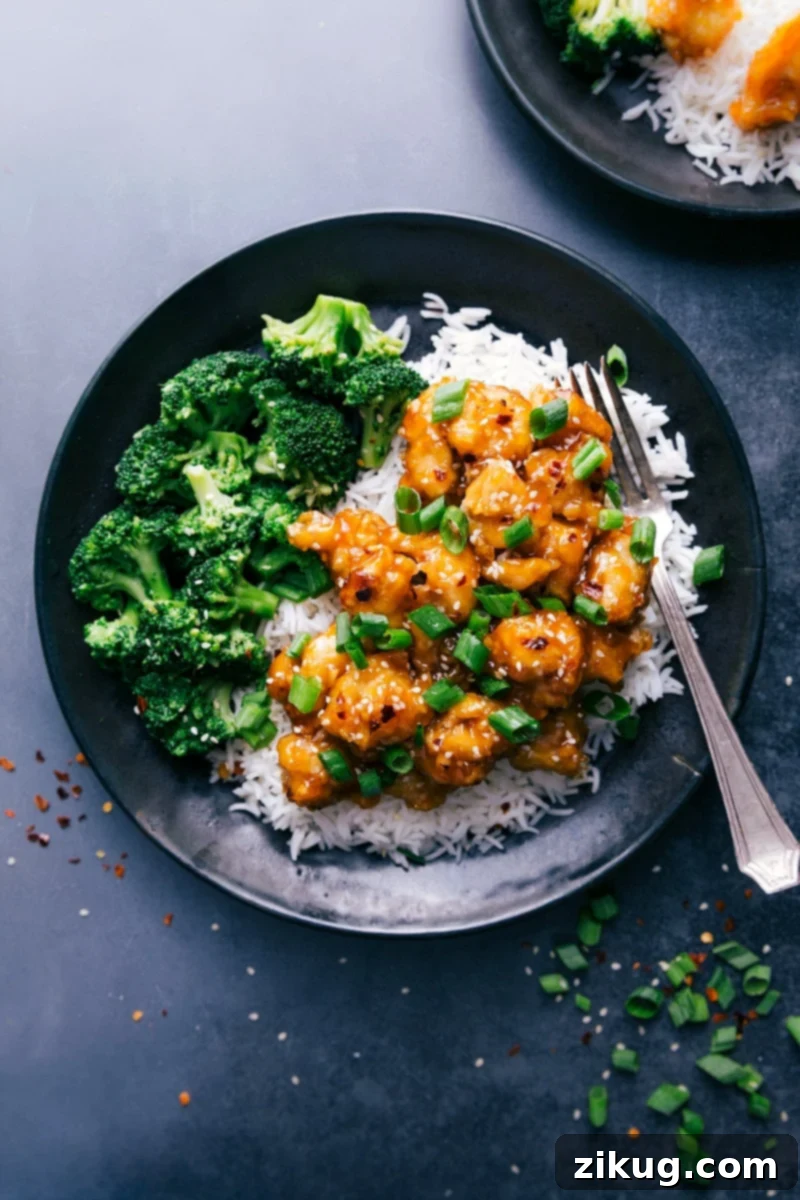 Delicious Orange Chicken served with fluffy white rice and steamed broccoli florets, garnished with sesame seeds and green onions.