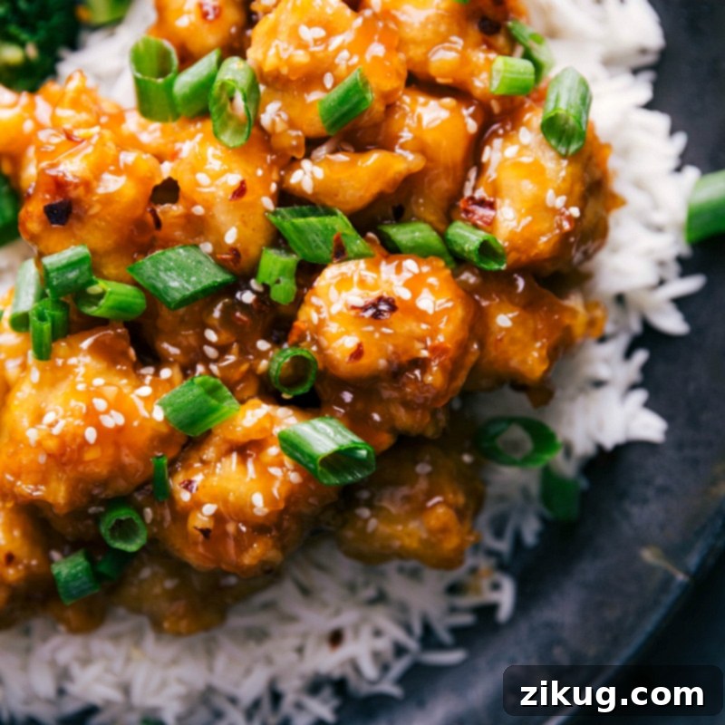 Homestyle Orange Chicken, beautifully plated with fluffy white rice, and garnished with fresh green onions and toasted sesame seeds for an appetizing finish.