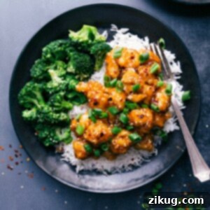 A bowl of delicious Orange Chicken garnished with green onions and sesame seeds, ready to be served.