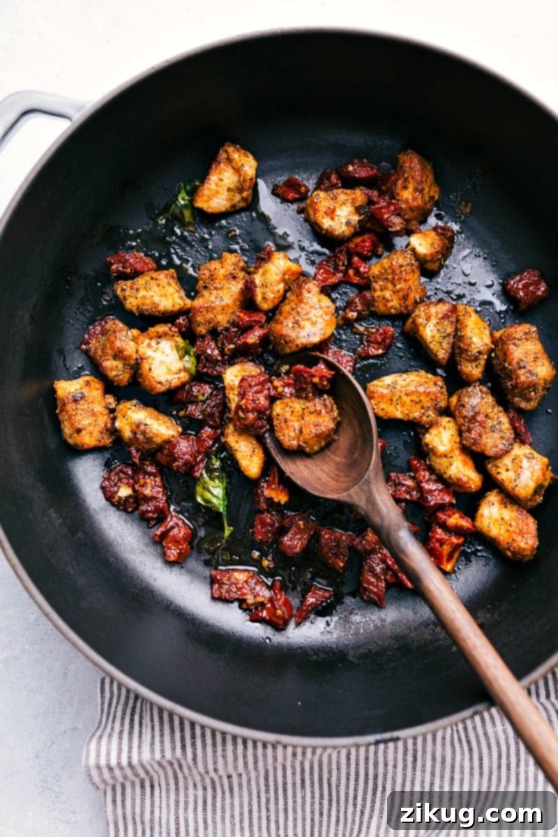 Sautéing Chicken and Sun-Dried Tomatoes for a Flavorful Pesto Tortellini Base Process shot showing chicken pieces and chopped sun-dried tomatoes being cooked together in a large nonstick pot, sizzling and browning.