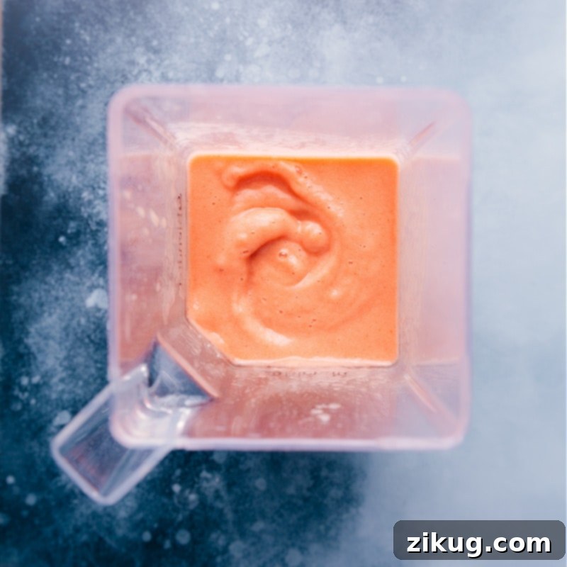 The vibrant blend of a Caribbean Passion Smoothie in motion, showcasing its thick and creamy texture directly from the blender. Overhead view of a perfectly blended Caribbean Passion Smoothie in a high-speed blender.