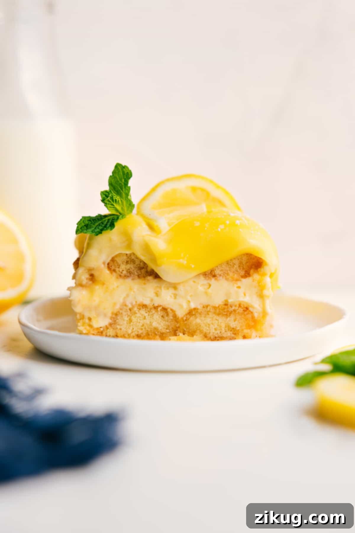 A Slice Of The Most Decadent And Delicious Lemon Tiramisu Lemon Tiramisu topped with fresh lemon curd, a lemon slice, and mint, showcasing its vibrant layers and inviting texture.