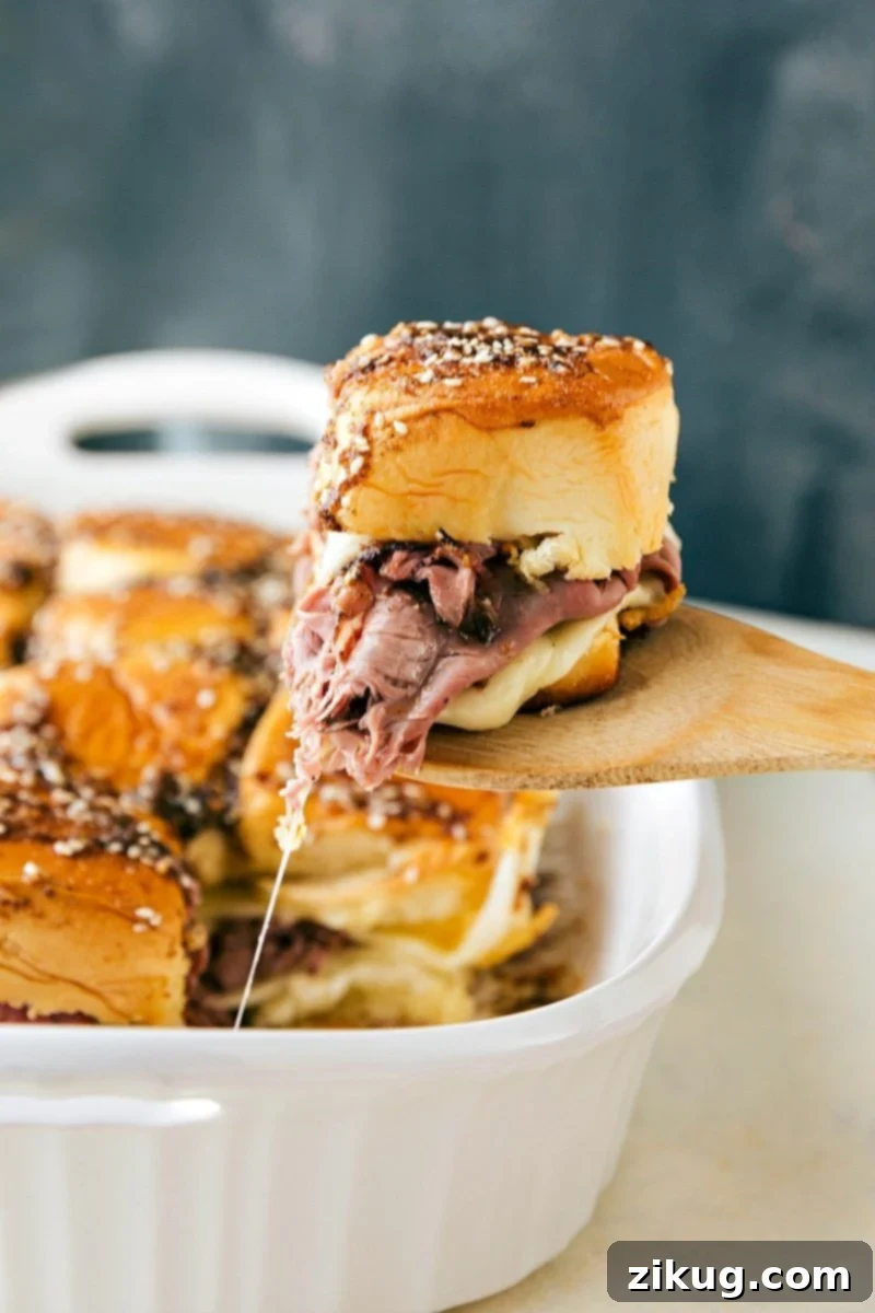 One Pan French Dip Sliders French Dip sandwiches fresh out of the oven with a spatula pulling one out.