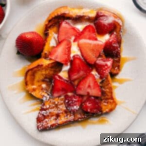 A stack of perfectly cooked French toast with whipped cream, strawberries, and caramel syrup.