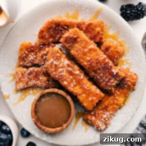 Close-up of freshly made Cinnamon Toast Crunch French Toast Sticks, golden brown and sprinkled with powdered sugar.