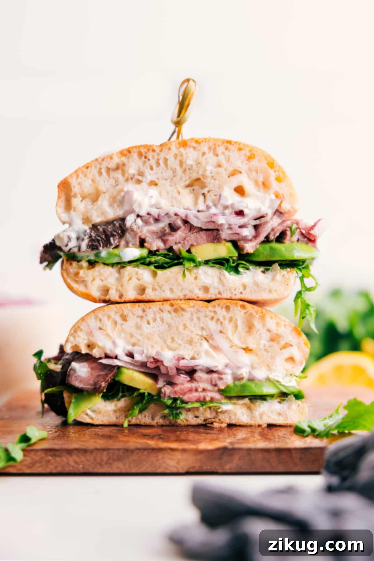 The Ultimate Steak Sandwich, piled high with tender steak, creamy aioli, avocado, arugula, and pickled onions on toasted ciabatta.