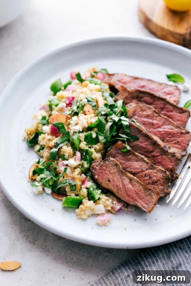 A hearty and colorful Spring Quinoa Salad with grilled steak, garnished with fresh herbs.
