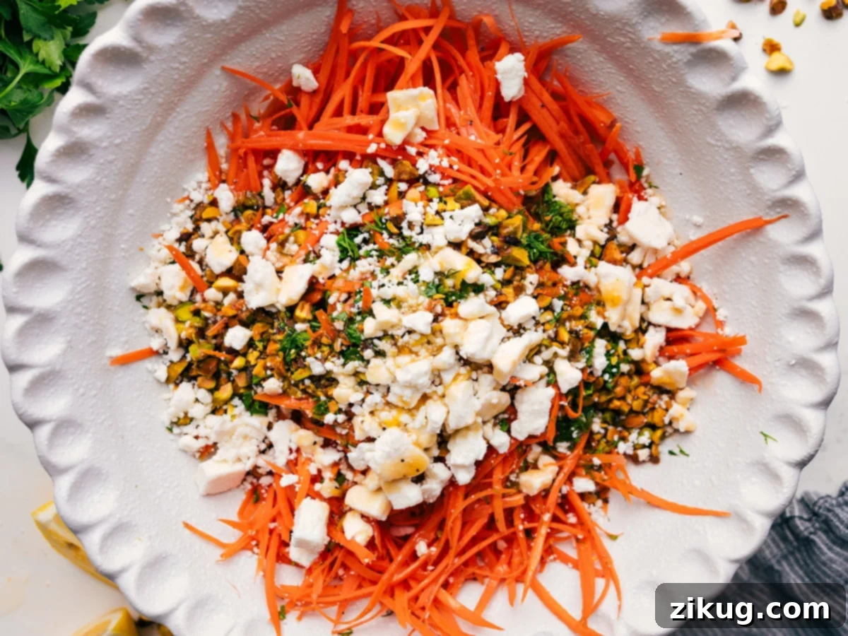 A large mixing bowl filled with freshly julienned carrots, chopped pistachios, and a generous scattering of fresh dill and parsley, all ready to be tossed with the zesty dressing.