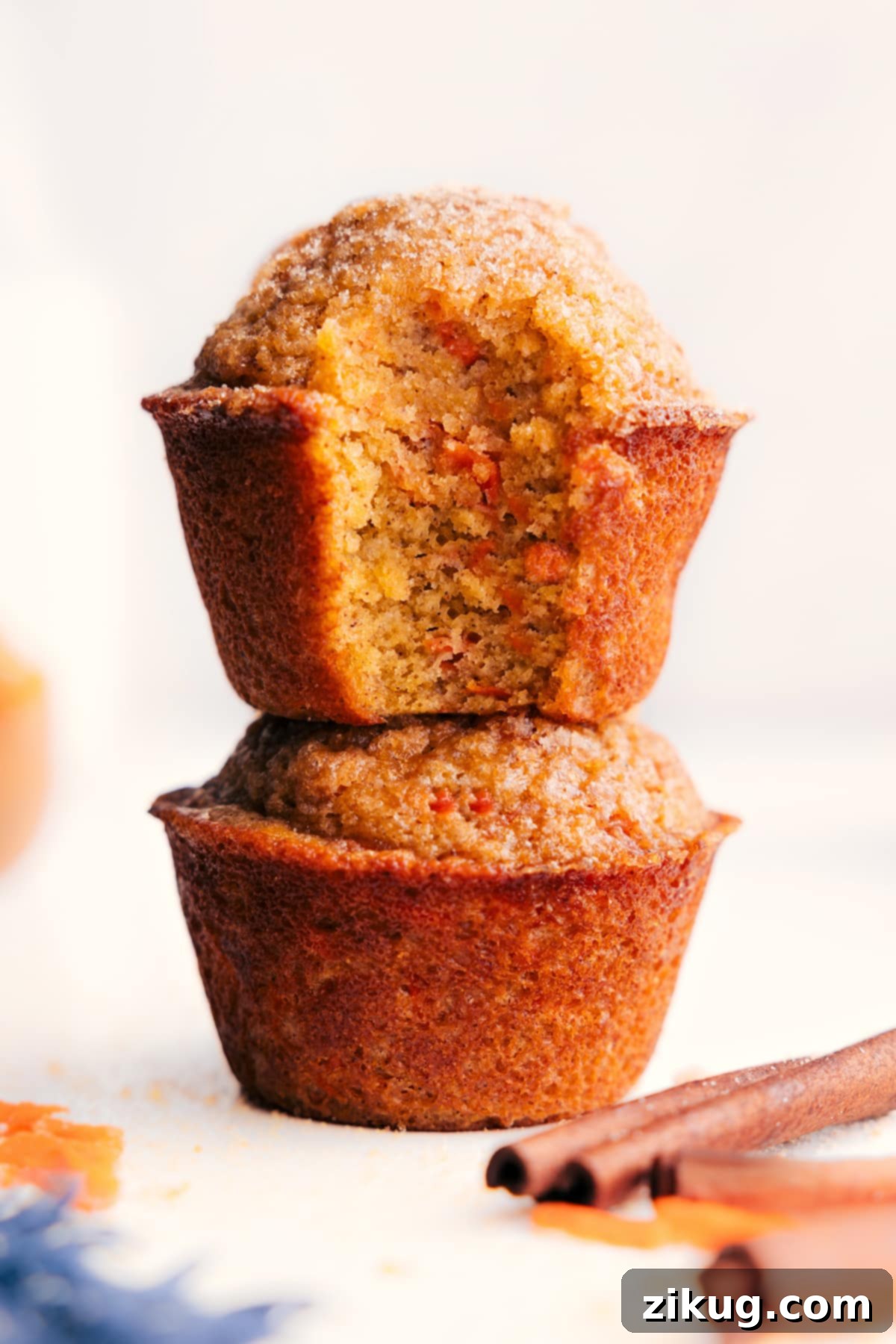 Flavorful And Delicious Healthy Carrot Muffins Stacked healthy carrot muffins, with one muffin having a bite taken out, revealing its soft, moist, and tender inside filled with grated carrots.