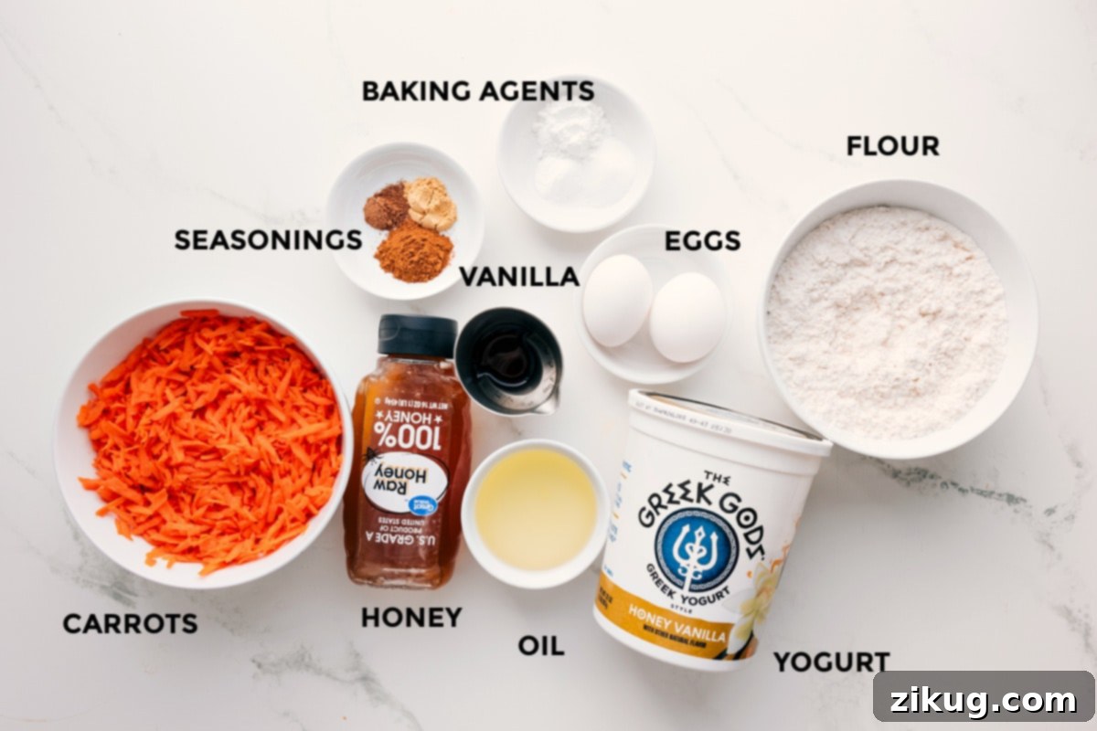 Ingredients In These Healthy Carrot Muffins All the essential ingredients for healthy carrot muffins, prepped and ready for assembly, including grated carrots, spices, honey, coconut oil, Greek yogurt, eggs, vanilla, flour, and leavening agents.