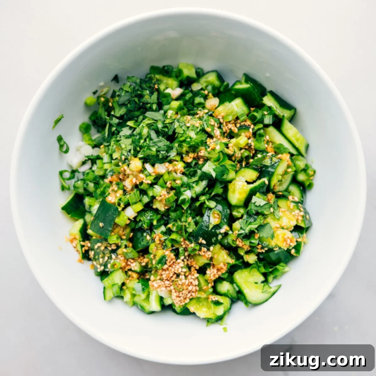 How To Make Smashed Cucumber Salad Smashed Cucumber Salad in a bowl with dressing and herbs ready to be tossed together