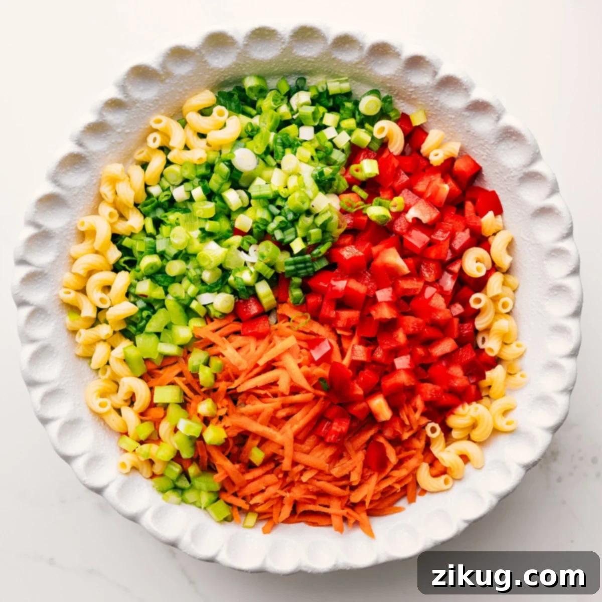 A large mixing bowl filled with all the delicious components of the Macaroni Salad—cooked elbow macaroni, brightly colored mixed vegetables, and the rich, creamy dressing—just before being thoroughly tossed together to combine the flavors.
