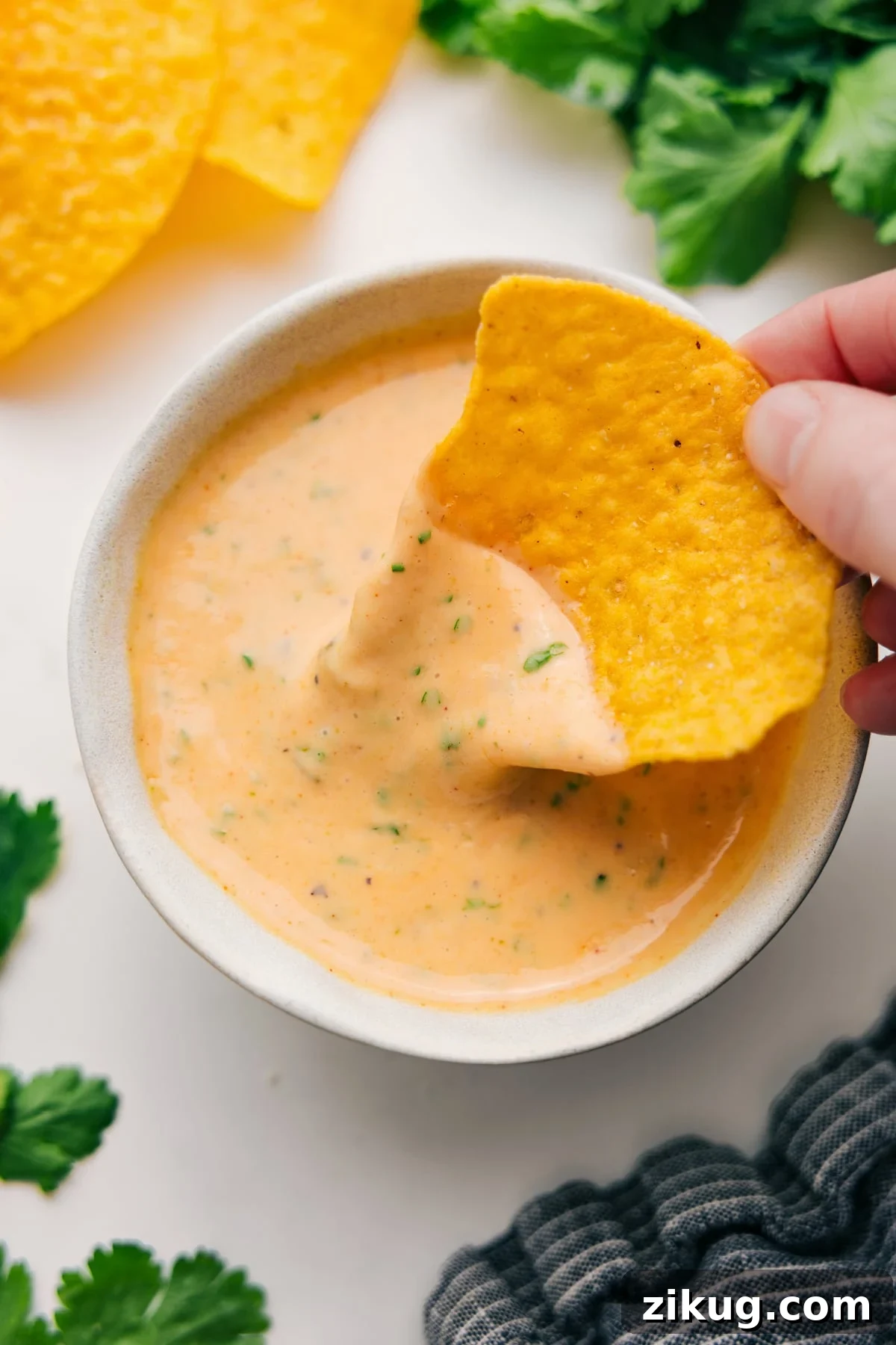 Smooth and Melty Queso Dip Queso dip in a bowl with a tortilla chip dipping into the melted cheese.
