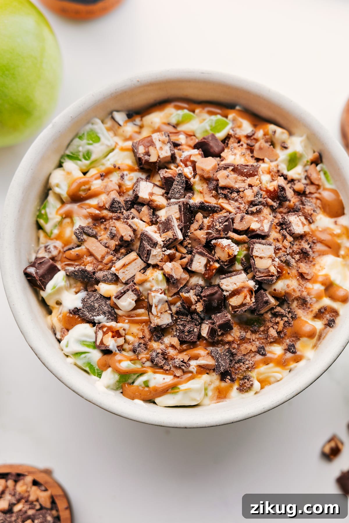 A Big Bowl Of The Most Delicious Snickers Salad Recipe Snickers Salad Recipe in a bowl topped with chopped Snickers and a drizzle of caramel sauce