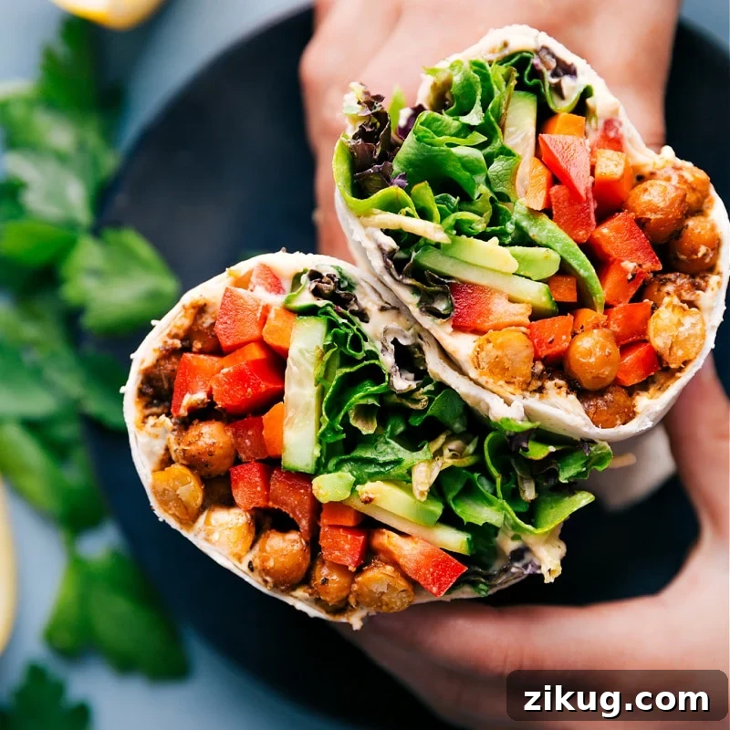 30-Minute Hummus Wrap Hummus wrap cut in half, showing chickpeas, fresh veggies, and sauce inside.
