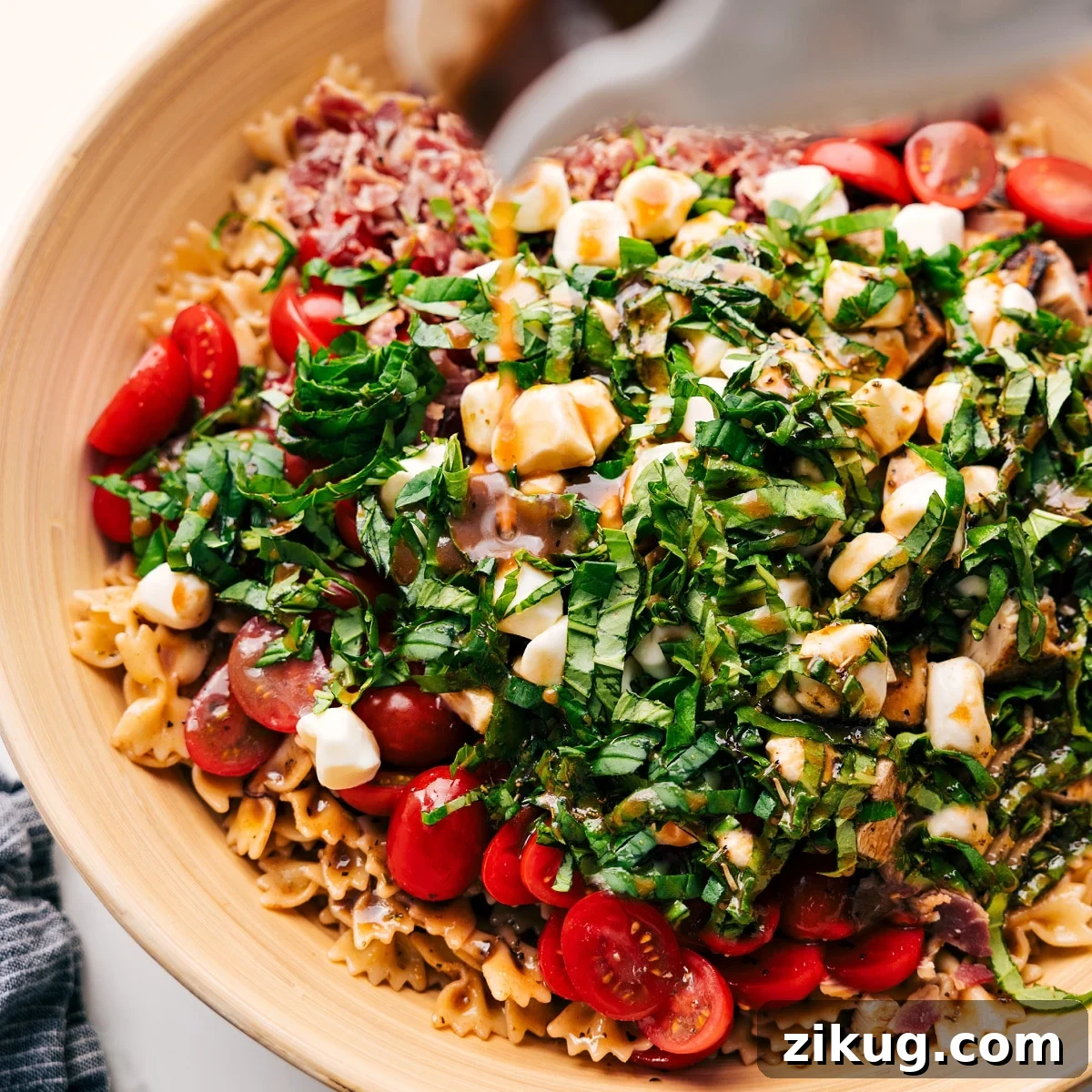 How To Make This Caprese Pasta Salad Dressing being poured over Caprese Pasta Salad in a large bowl before being tossed together.